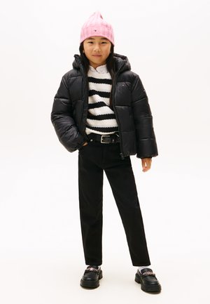 Giacca a vento nera, maglione a maglia a righe bianche e nere, pantaloni neri, berretto rosa a costine e scarpe platform nere con dettagli a catena.