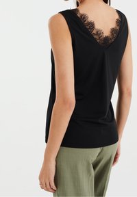 Svart ärmlös topp med spetsdetaljer vid den V-formade halsringningen och en slät tygtextur, som kombineras med ljusgröna, löst sittande byxor.