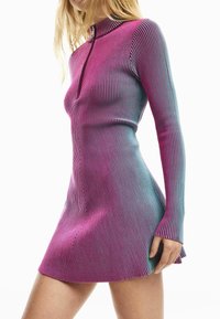 Muotoiltu mekko, jossa on korkea kaulus ja pystysuuntaiset vaaleanpunaiset ja siniset raidat. Valmistettu ribbineuloksesta, siinä on etuvetoketju ja pitkät hihat.