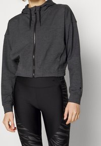 Avklippt grå hoodie med framdragkedja, huva och elastisk nederkant; kombinerad med svarta leggings med ett subtilt tigermönster.