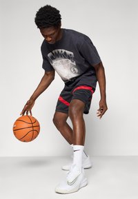 Černé grafické tričko s designem basketbalu, černé šortky s �červenými akcenty, bílé tenisky Nike a basketbal, na neutrálním pozadí.