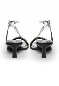 Sandalias de tacón alto plateadas con tiras, con suela negra, que presentan rhinestones decorativos a lo largo del borde curvado y un acabado brillante y elegante.