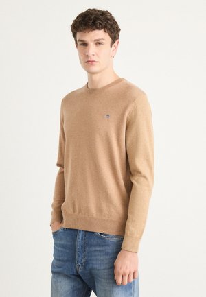 Light brown crew neck sweater made from soft material, featuring ribbed cuffs and hem, with a small logo accent on the chest.