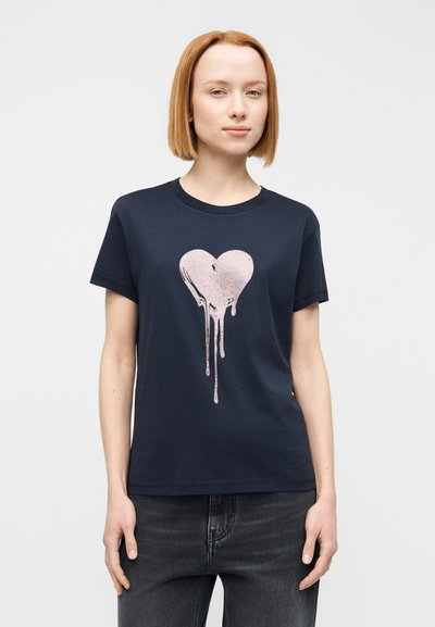Μπλε βαμβακερό μπλουζάκι ναυτικού τύπου με γραφικό από καρδιά που στάζει σε ροζ χρώμα. Με κοντά μανίκια, στρογγυλή λαιμόκοψη και άνετη γραμμή.