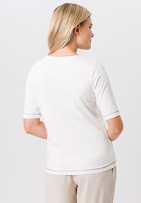Witte korte mouwen shirt met een ronde halslijn, voorzien van roze stikselaccenten op de mouwen en de zoom. Glad materiaal, aansluitend ontwerp.