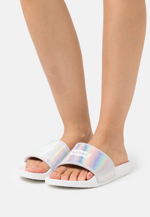 Des pieds chaussés de sandales blanches à brides iridescentes arborant le logo Levi's, sur un fond blanc.