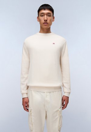 Cream-colored sweatshirt with a round neck, ribbed cuffs, and hem. Features a small red and white logo on the chest. Worn with light pants.