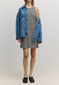 Jeansowa kurtka, jasnoniebieska, w oversize'owym kroju, noszona rozpięta na czarno-białą w paski sukienkę do kolan, zestawiona z czarnymi butami wsuwanymi.