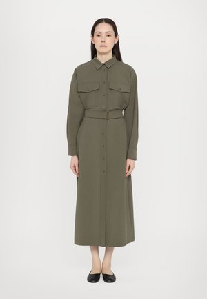 Olivgrünes, langärmliges Hemdkleid mit zwei Brusttaschen und einem taillierten Bund. Knopfleiste vorne und knöchellanger Saum. Schwarze Flats.