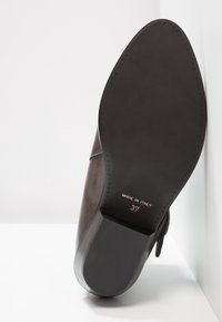 Brązowa skórzana podeszwa buta z wysmukłym noskiem, gładką teksturą, minimalnym bieżnikiem oraz wytłoczonymi detalami: "MADE IN ITALY" i rozmiar 37.