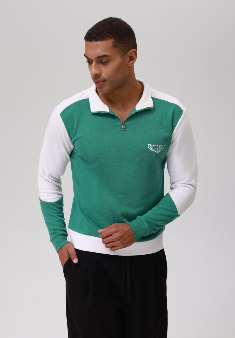 Pullover de media cremallera en verde y blanco, hecho de una tela texturizada. Presenta un diseño en contraste con puños acanalados y el logotipo bordado "ENDURANCE".