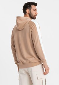 Huvtröja i beige med vita sidostripes. Tillverkad av mjukt tyg, med en avslappnad passform och ribbade manschetter för komfort.