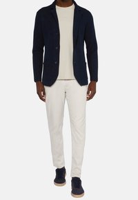 Námořnický texturovaný blejzr s dvěma předními kapsami, béžové tričko, bílé kalhoty a námořnické tenisky s gumovou podešví. Neformální vrstvený outfit.