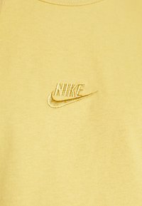Gult stof med lille broderet Nike-logo i matchende gult garn centreret på overfladen.