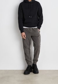 Felpa nera in cotone con tasca frontale, abbinata a pantaloni della tuta grigi con tasche laterali e polsini elastici. Scarpe da ginnastica nere con lacci incluse.