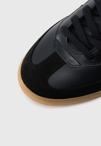 Μαύρο δερμάτινο και σουέντ αθλητικό παπούτσι με στρογγυλή μύτη, υφασμάτινες λεπτομέρειες και σόλα από καουτσούκ. Διαθέτει μαύρα κορδόνια και ραφές.