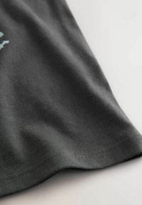 Dark gray cotton fabric with a smooth texture, featuring a curved hem and stitching along the edge. Simple design, no additional patterns or accents.