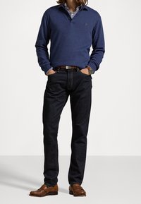 Tummansininen pitkähiha-paita kauluksella, yhdistettynä tummiin farkkuihin. Ruskeat nahkakengät, joissa on yksityiskohtaisia ompeleita, sekä näkyvä vyö.