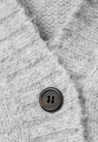 Tissu de pull en maille grise présentant un motif texturé et un bouton sombre à deux trous, offrant une apparence chaude et douce.