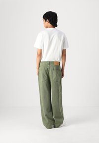 Calças largas verdes de ganga, com dois bolsos traseiros e um rótulo de pele castanha na cintura. Combinadas com uma t-shirt branca.