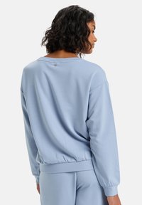 Světle modrá mikina s uvolněným střihem, žebrovanými manžetami a spodním lemem. Hladký materiál s jemným detailem na zádech poblíž výstřihu.