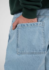 Hele sinised teksad suure tagataskuga. Kangas on pehme, kerge tekstuuriga ning servi mööda nähtavate õmblustega.