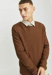 Suéter de crewneck marrón con textura y puños acanalados, superpuesto a una camisa de cuello con un ligero diseño a cuadros. Diseño simple y casual.