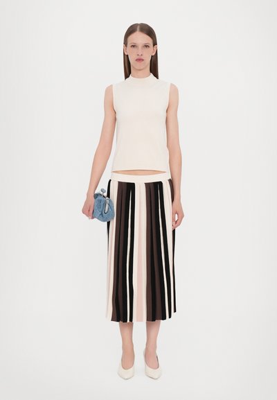 Knit sleeveless top in off-white, paired with a long, multicolored striped skirt. Blue knitted clutch with a drawstring. White heels.