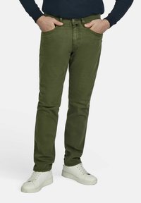 Chinos vert olive avec une coupe slim, quatre poches et une fermeture à bouton, associés à des baskets blanches pour le contraste. Texture en coton lisse.