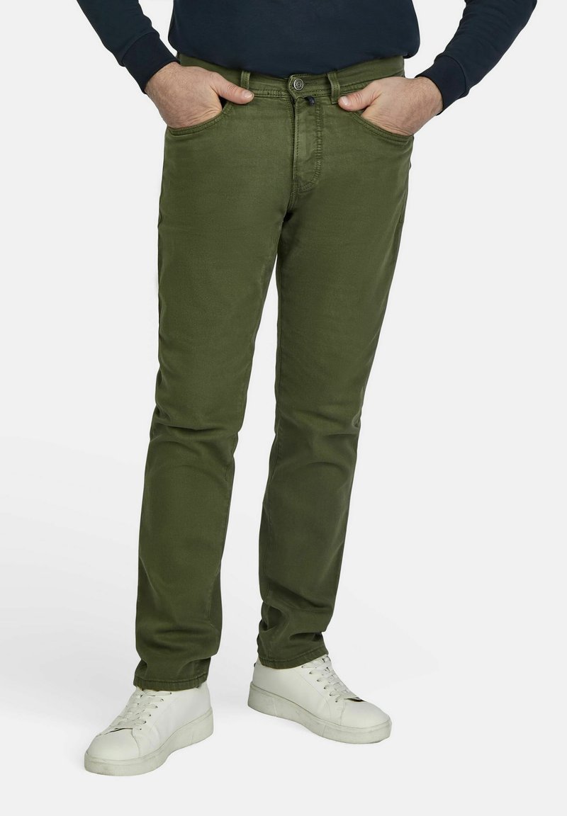Chinos vert olive avec une coupe slim, quatre poches et une fermeture à bouton, associés à des baskets blanches pour le contraste. Texture en coton lisse.