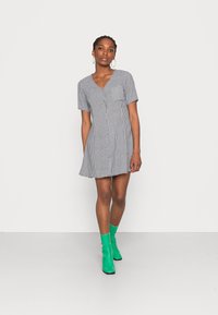 Vestido xadrez preto e branco com mangas curtas, decote em V e bainha rodada. Combinado com botas de tornozelo verde brilhante.