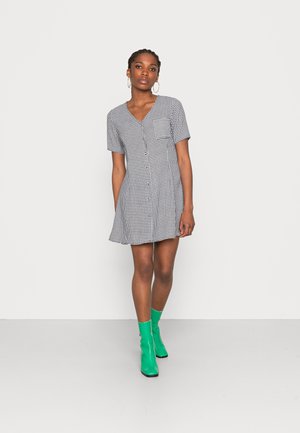 Vestido xadrez preto e branco com mangas curtas, decote em V e bainha rodada. Combinado com botas de tornozelo verde brilhante.