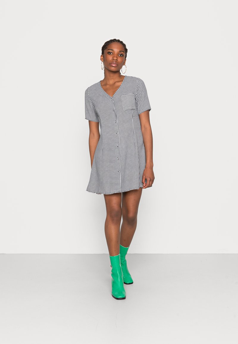 Vestido xadrez preto e branco com mangas curtas, decote em V e bainha rodada. Combinado com botas de tornozelo verde brilhante.