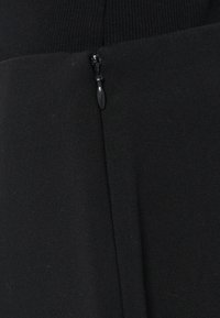 Tessuto nero con una texture liscia, caratterizzato da un breve dettaglio con zip. La cucitura è pulita e il tessuto appare leggermente elasticizzato.