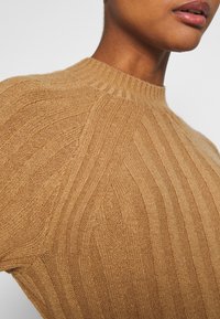 Maglione lavorato a maglia in beige caldo con una trama a coste e colletto corto. Presenta linee diagonali e un design aderente.