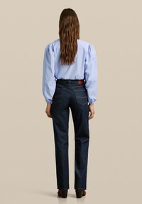 Blauwe en wit gestreepte blouse met puffed sleeves, gecombineerd met donkerdenim hoge taille jeans met achterzakken en rechte pijpen.