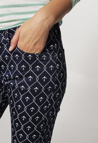 Námořnické kalhoty s bílým námořnickým vzorem kotvy v diamantovém uspořádání. Obsahují boční kapsu a hladkou texturu látky.