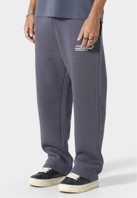 Grå sweatpants med lige ben, elastisk talje, sidelommer og "IRASUTO STUDIO" logo i hvidt på venstre lår.