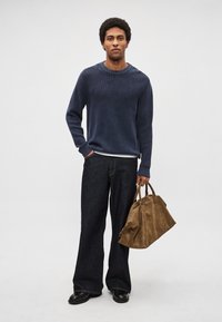 Camisola de malha azul-marinho com nervuras, combinada com jeans largos de ganga escura. Mala de pele castanha na mão, com sapatos pretos a completar o conjunto.