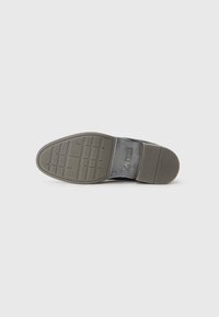 Suela de zapato de cuero negro con un patrón de agarre texturizado. Presenta una forma redondeada, con dimensiones estándar y un acabado suave.