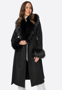 Schwarzer langer Mantel mit einem plüschigen Kunstfellkragen und -manschetten, glatter Textur, einem Knopfverschluss und einer taillierten Silhouette.