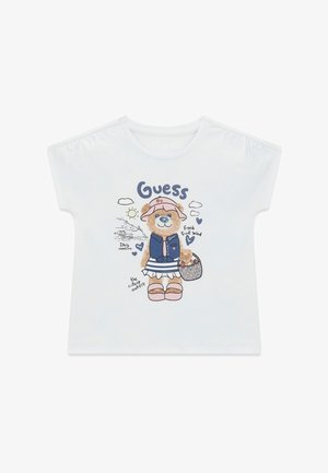 Maglietta bianca per bambini con un orso che indossa un cappello, un gilet, una gonna a righe, sandali, tiene un cestino e il testo con le parole "Guess" e "Vacanze in Italia".