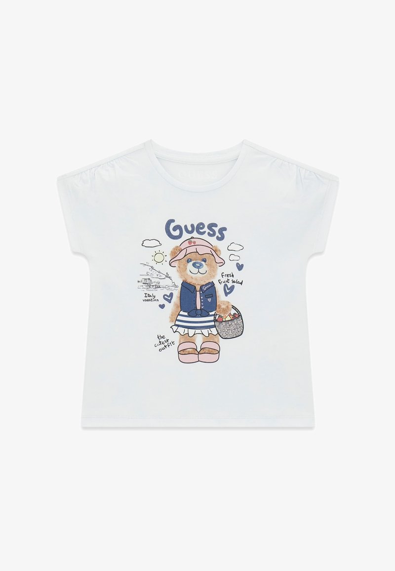 T-shirt blanc pour enfants avec un ours portant un chapeau, un gilet, une jupe rayée, des sandales, tenant un panier, avec le texte incluant "Guess" et "Vacances en Italie".