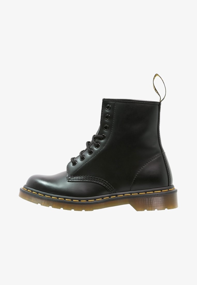 Bottine noire en cuir à lacets avec surpiqûres jaunes, semelle épaisse translucide et languette à l'arrière, sur fond blanc.