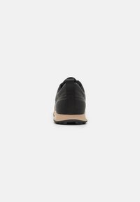Black athletic shoe with a textured upper, a pull tab at the heel, and a beige midsole. Features a rounded toe and treaded outsole.