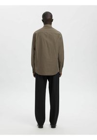 Brun rutete skjorte med lange ermer og krage, kombinert med løse svarte bukser. Jevn tekstur og standard passform, vist bakfra.