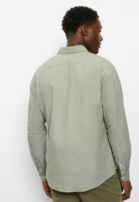 Hellgrünes langärmeliges Hemd mit klassischem Kragen, geknöpften Manschetten und einem dezenten strukturierten Stoff sowie einem abgerundeten Saum.