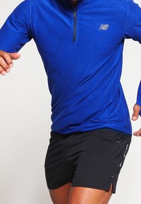 Blå långärmad atletisk topp med kvart dragkedja och svarta shorts. Har en subtil logo och fukttransporterande tyg för komfort.