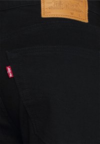 Jeans de mezclilla negra con una etiqueta de cuero que presenta detalles en relieve. Etiqueta roja de Levi's en el bolsillo trasero. Patrón de costura curvado distintivo.
