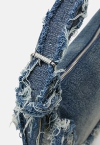 Denim torba s franjami. Modra barva, teksturirana tkanina, srebrni okovi z pritrjenim sponko. Kvadratna oblika z zadrgo.